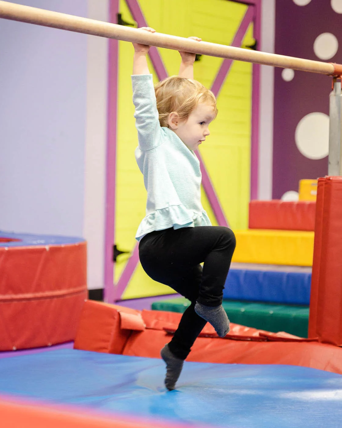 A kid swinging from Romp n' Roll gym equipment - safe kids fitness classes.