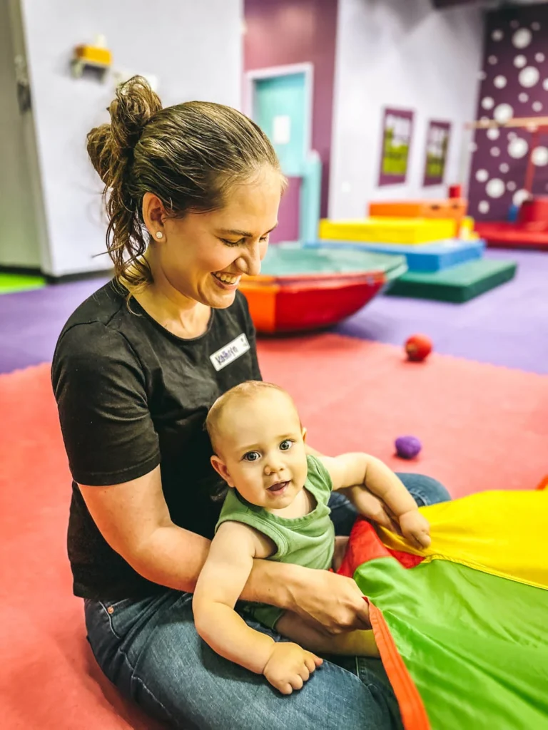 A mom and a baby playing with a colorful parachute.