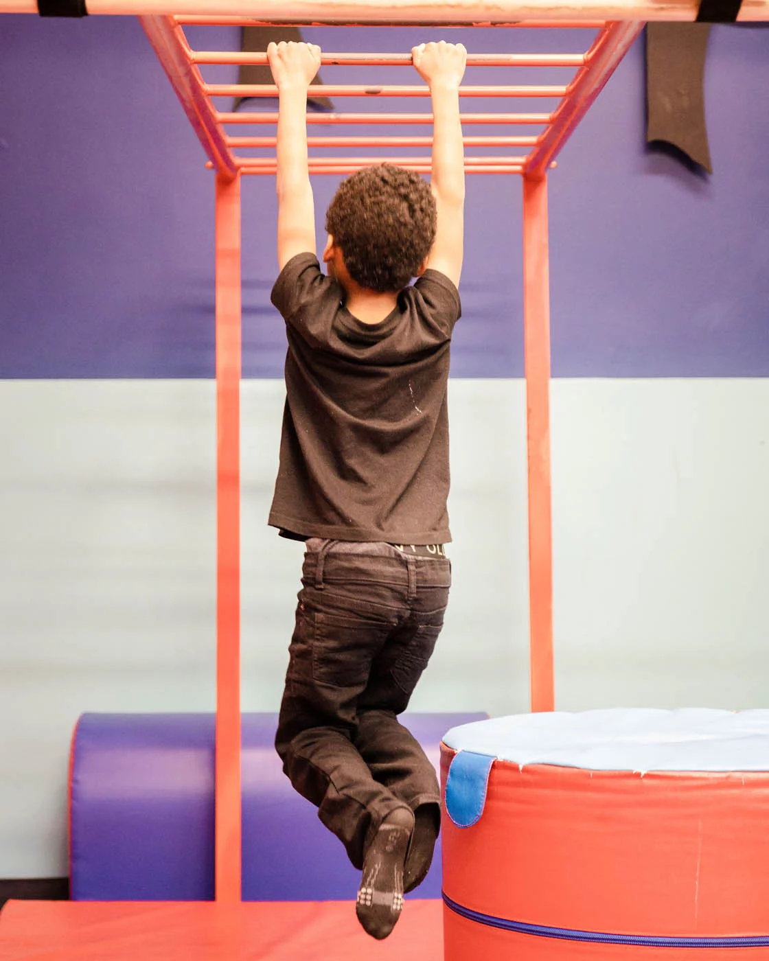 A boy swinging on monkey bars in our kid-safe gym at Romp n' Roll.