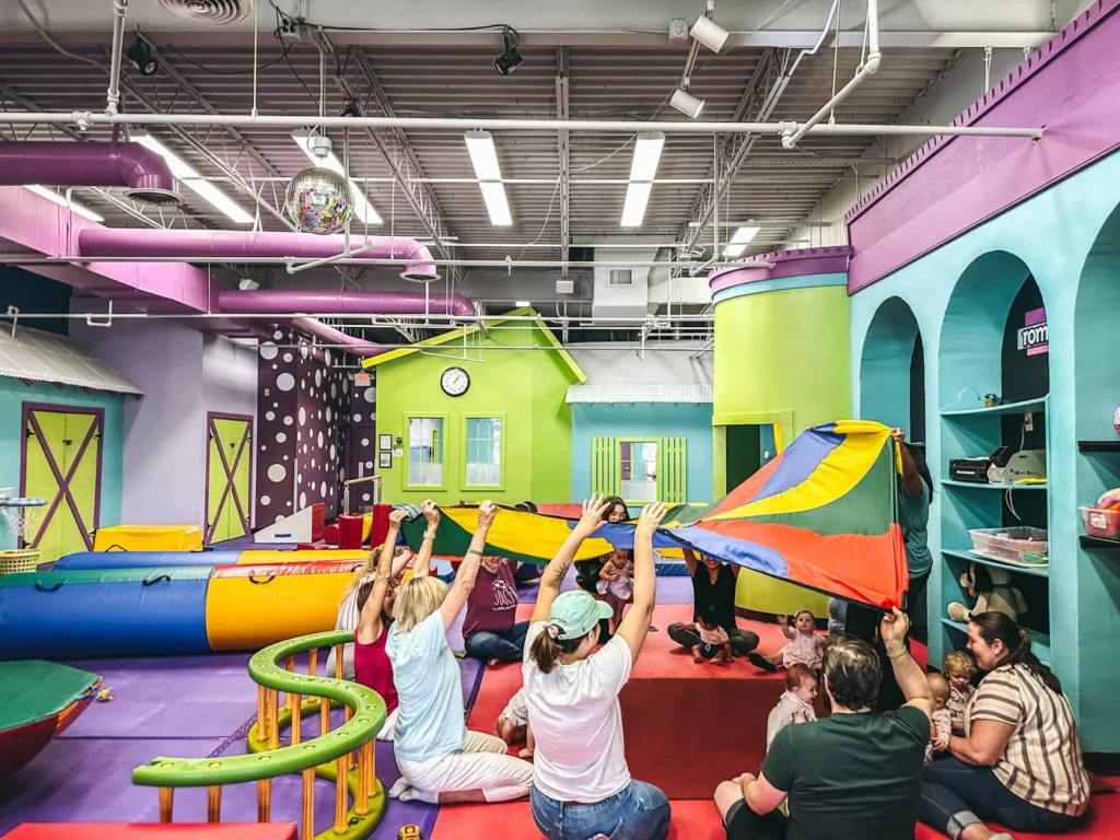 Adults and kids at Romp n' Roll enjoying the fun of parachute playtime in our gym!