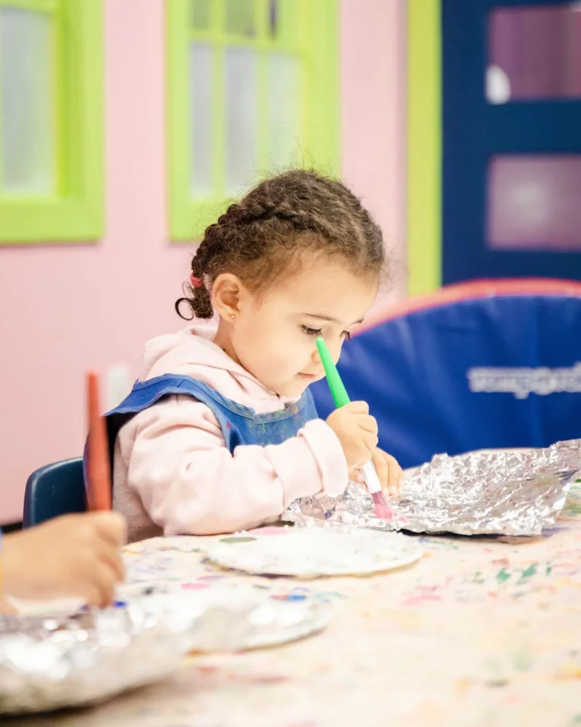 A girl at a Romp n' Roll art classes for kids using a paint brush.